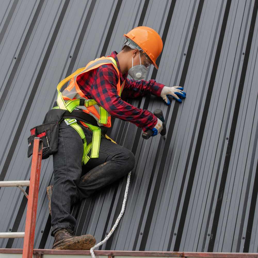 a roofer wearing a hard hat and safety equipment working on metal siding