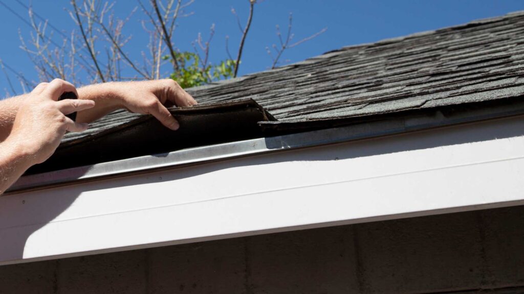 lifting shingles to show a metal flashing on the edge of a roof